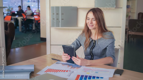 Business woman using app on the touch screen tablet. On her desk documets and charts with sales report photo