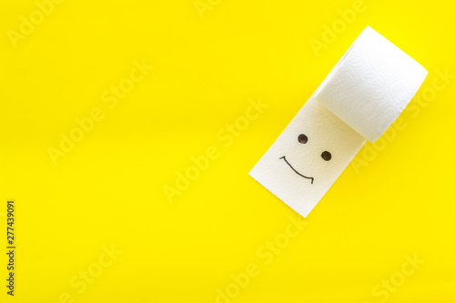 Toilet paper roll with painted face for proctology diseases concept on yellow background top view mock up