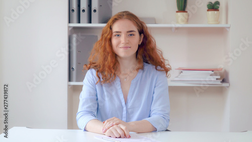 Photography Portrait successful business woman with curly redheaded long hair sitting at the white desk in office sign document