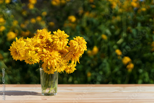 Summer rustic concept. Yellow flowers golden ball in a faceted glass cup. A table made of wooden planks. Beautiful yellow green bokeh. There is a copy space