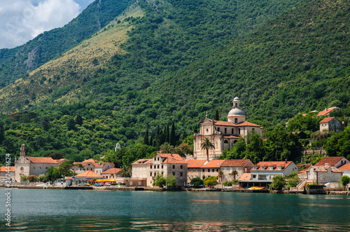 View of the seaside ancient city on the Adriatic Sea shore. Houses with red-tiled roofs and an old church at the foot of the green mountain. Seascape.