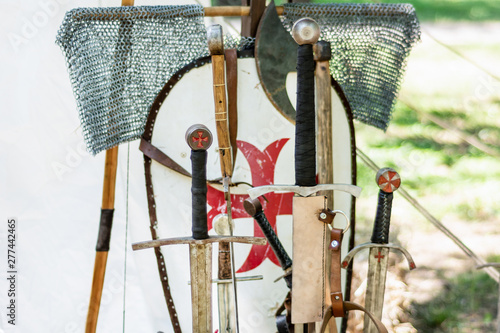 A medieval old group of swords and knights equipment. Close up of handles sword and blurred shield in the background. Medieval and historical concept. Selective focus. photo