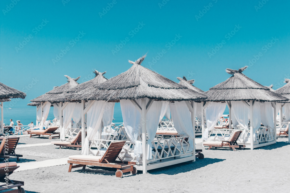 Several beautiful tents from the sun on a sandy beach, against the background of a beautiful turquoise blue sky.