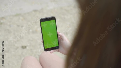 Woman using smartphone with Green Mock-up Screen Sitting on bench in Eiffel Tower park, Touch screen with Tracking Markers. Browsing Internet, Watching Media Content, Videos, Blogs, Social Networks.