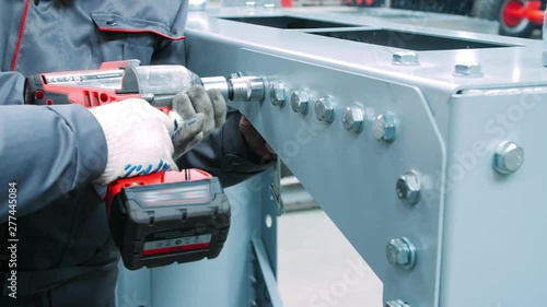 Tightening bolts on metal surface of industrial machine. Using screwdriver