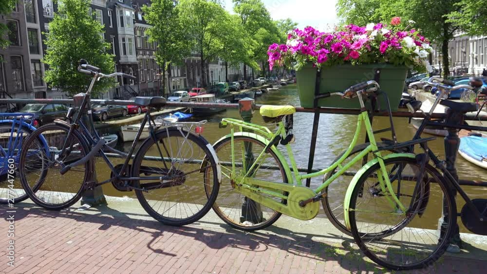 Idyllic cityscape with bikes parked on bridge decorated by flowers over Amsterdam canal. Ships along the sides of waterway. antique buildings, Amazing view of flourishing European city on sunny day