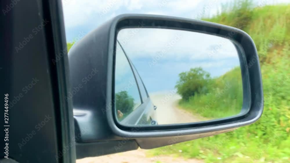 View in the side mirror, the car moves off-road in the village on a sunny day View in the side mirror, the car moves off-road in the village on a sunny day