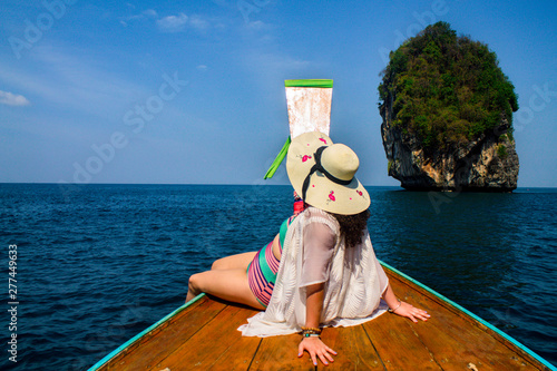 Young girl sitting on the bow of a boat in Thailand. Crystal clear water and rocky mountains. Tropical beach