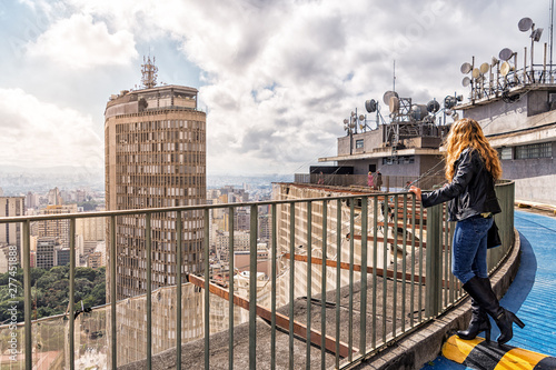 Blond Brazilian Woman Looking at the São Paulo City Skyline from the Roof of COPAN, during visitation hours. COPAN is a Modern Design Building with 1.160 Residential Apartments.