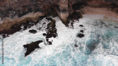 Wallpaper Mural aerial cinematic view of broken beach circular rock formation with ocean waves crashing into the centre on edge of indonesian island during warm overcast day with blue water Torontodigital.ca