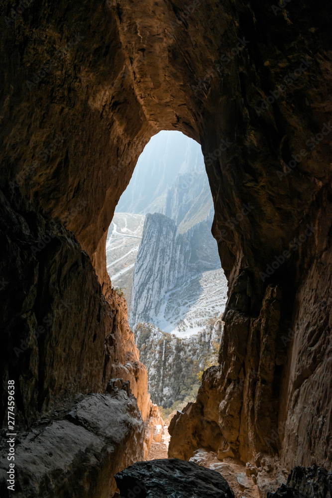 Rocky mountain range view from inside an orange-rock cave illuminated by sunlight