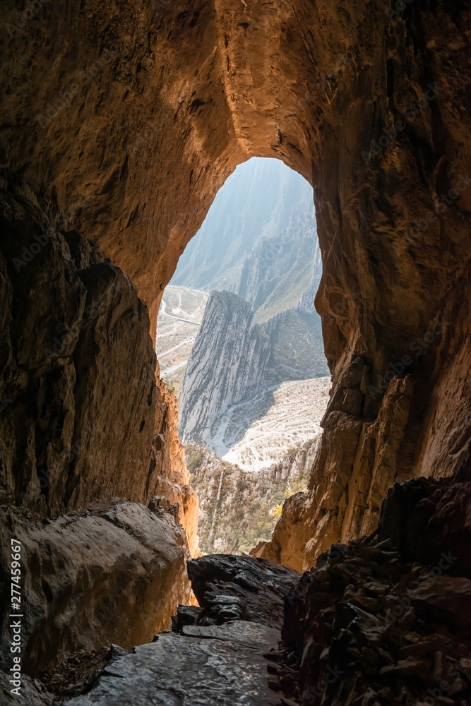 Rocky mountain range view from inside an orange-rock cave illuminated by sunlight