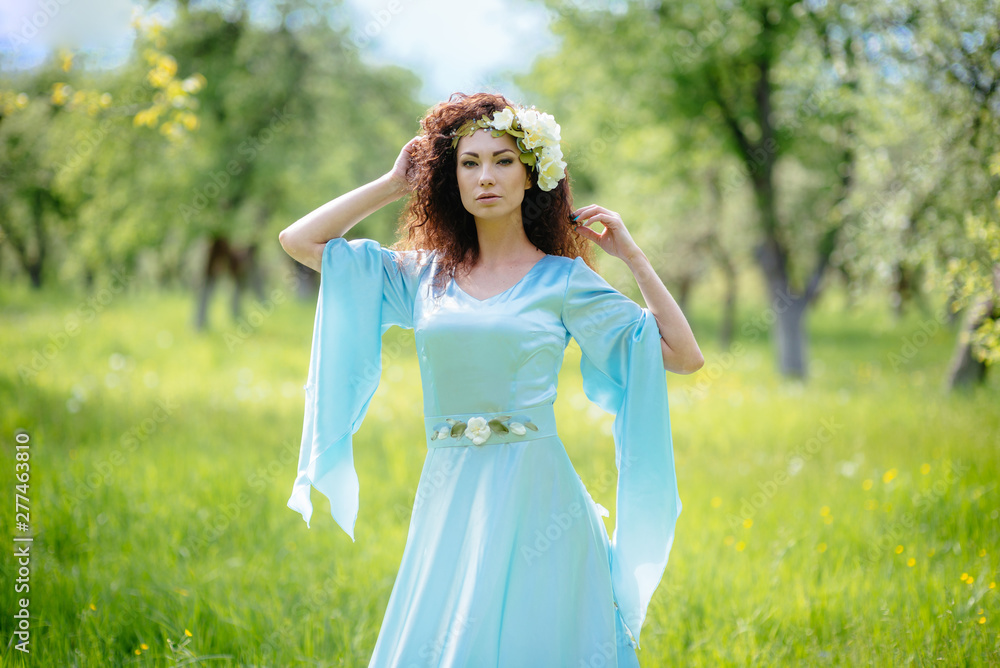 Beautiful girl is standing in the spring apple garden in a long dress