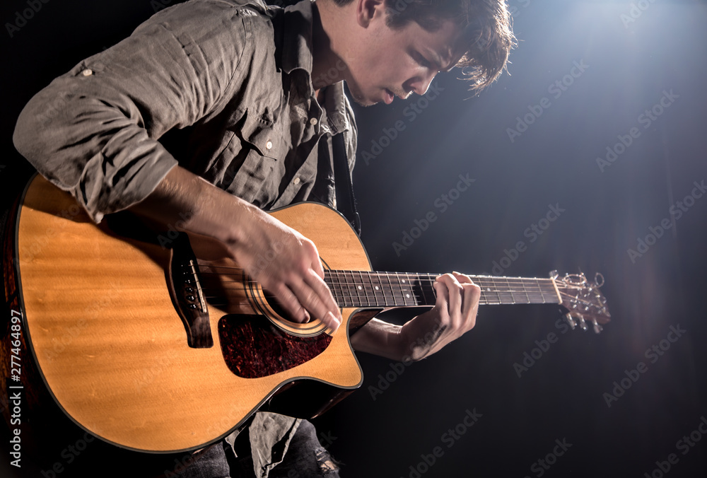 Obraz premium Guitarist, music. A young man plays an acoustic guitar on a black isolated background