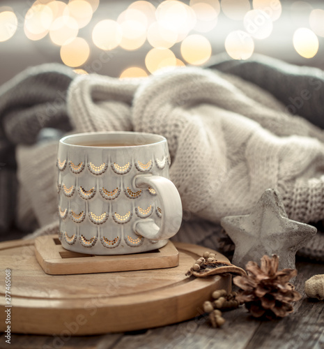 Coffee cup over Christmas lights bokeh in home on wooden table with sweater on a background and decorations. Holiday decoration