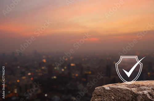 Canvas Print Security shield with check mark flat icon on rock mountain over blur of cityscap