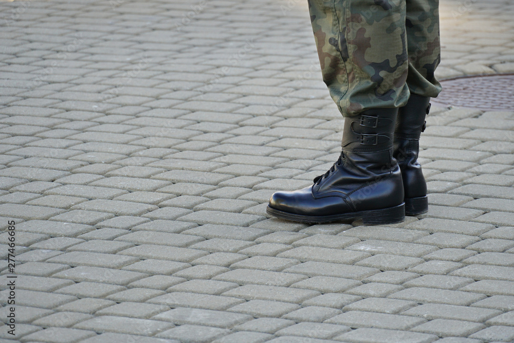 leg of male soldier with black top boot on grey footpath background leg of male soldier with black top boot on grey footpath background