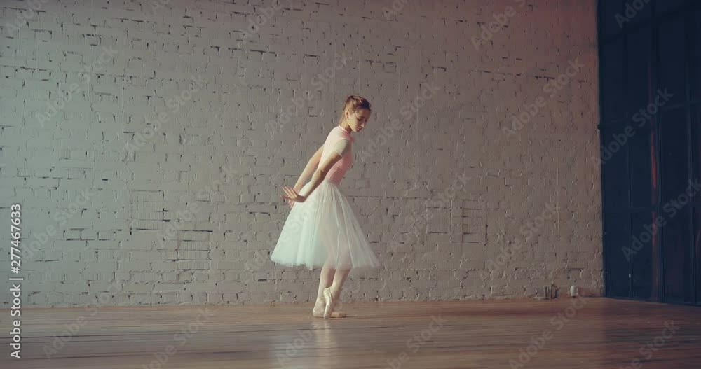 Beautiful young ballerina dancing in the studio. Smooth movement of the arms, raising the leg up.