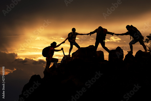 Silhouette of Hikers climbing up mountain cliff. Climbing group helping each other while climbing up in sunset. Concept of help and teamwork  Limits of life and Hiking success full.