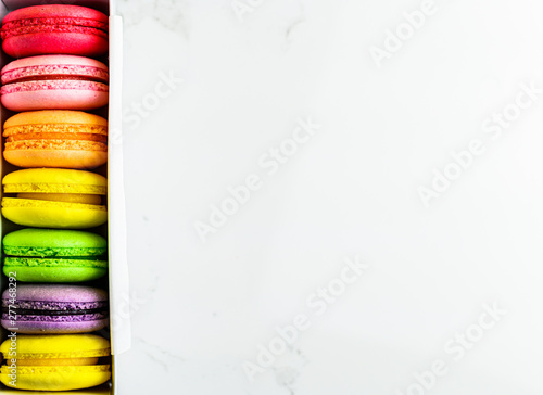 A french sweet delicacy, macaroons variety closeup. Colourful French Macaroons in box on modern table top view with copy space for your design.
