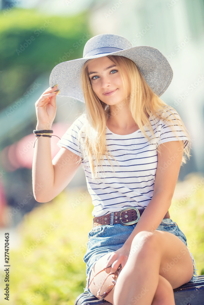 Summer portrait of young beautiful woman in hat sitting on bench in park