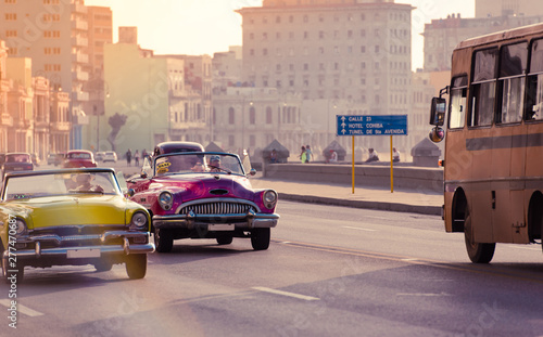 Gelber und pink farbener Cabriolet Oldtimer fahren auf der Promenade el Malecon in Havanna Stadt Kuba an der historischen Häuserfront vorbei - Serie Kuba Reportage