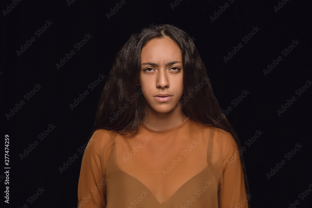 Fototapeta premium Close up portrait of young african-american woman isolated on black studio background. Photoshot of real emotions of female model. Facial expression, human nature. Sadness, look serious.