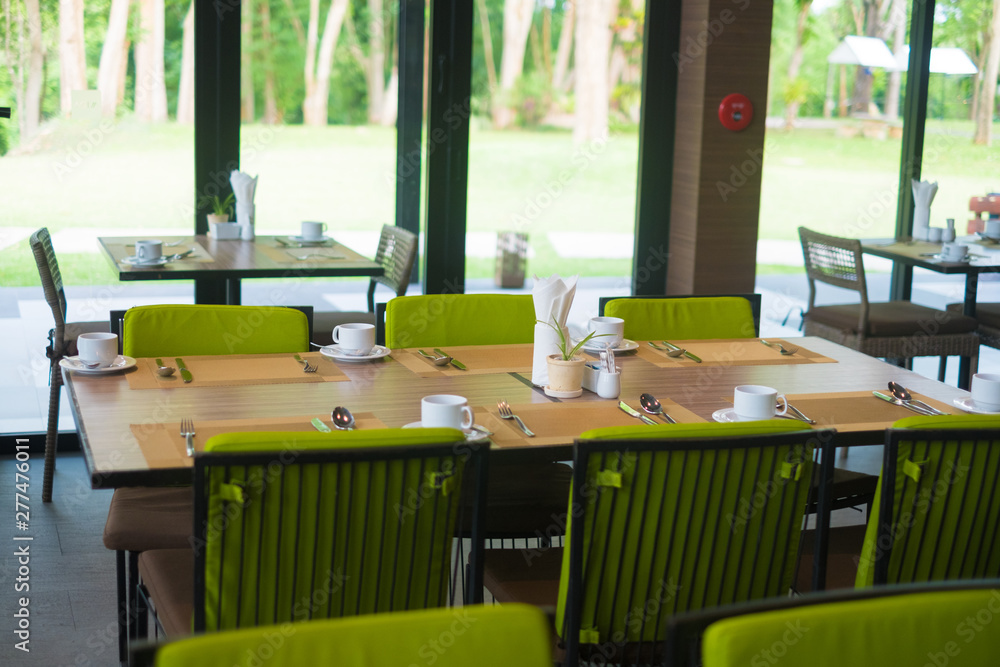 Fototapeta premium Empty restaurant part of hotel with table and armchair near windows and garden view.