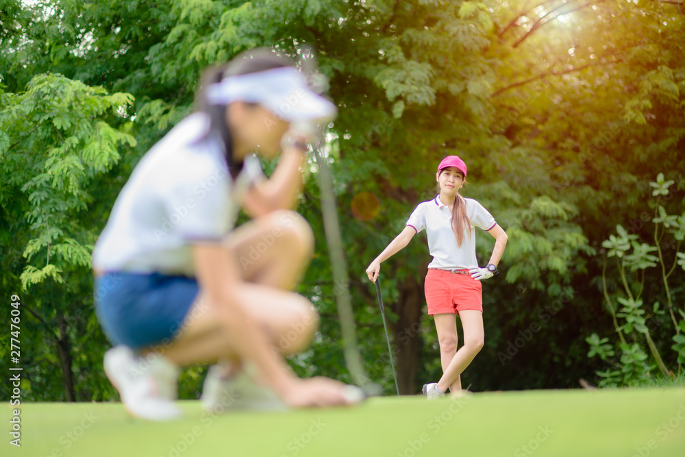 woman golf player looking waiting for opponent competitor or golf mate laying golf ball on the green of the golf course for final score putting