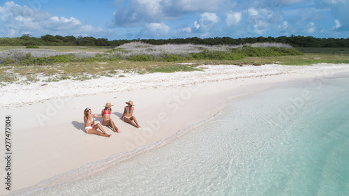 three women Sitting on the white sand caribbean Beach. Drone Aerial View