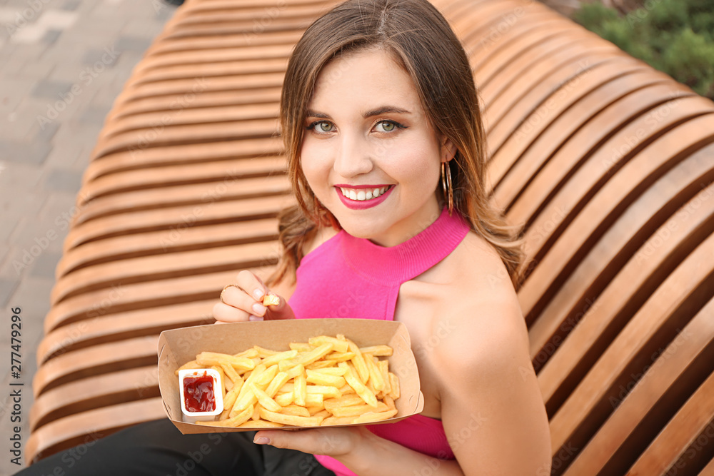 Beautiful young woman eating tasty french fries outdoors Beautiful young woman eating tasty french fries outdoors