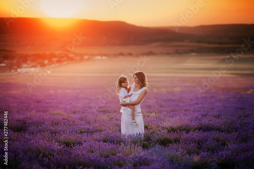 Mom and daughter in beautiful white dresses in a lavender field in the summer at sunset.