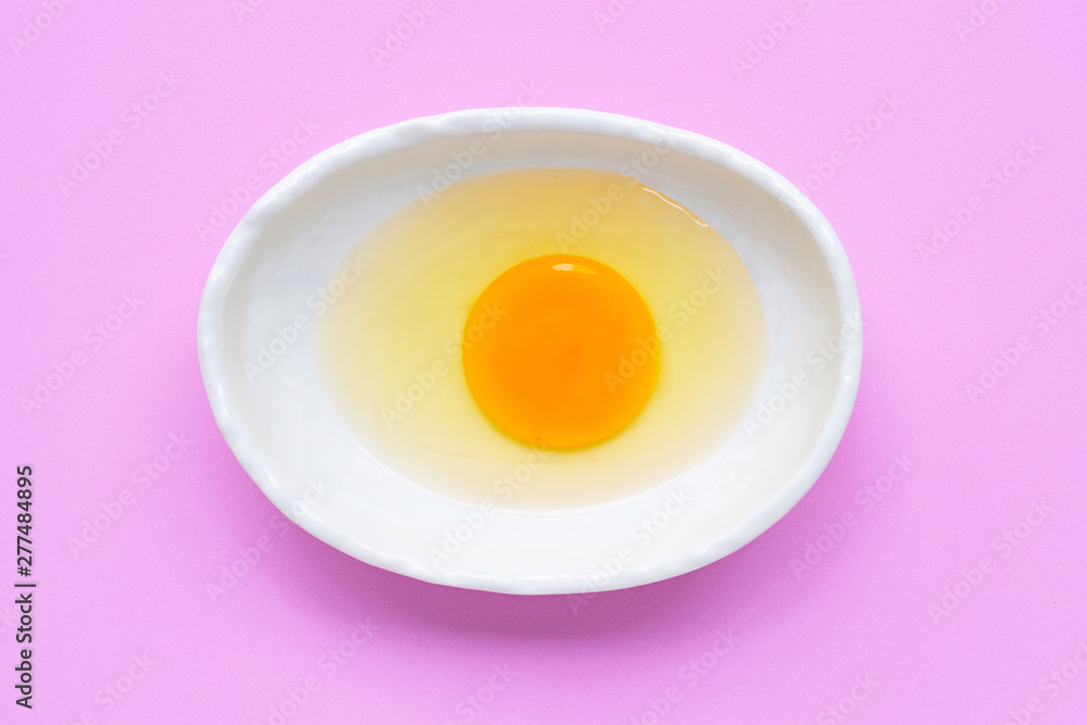 Egg yolk and white in a bowl on pink background. Egg yolk and white in a bowl on pink background.
