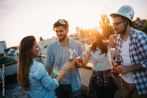 Young people partying on terrace with drinks at sunset