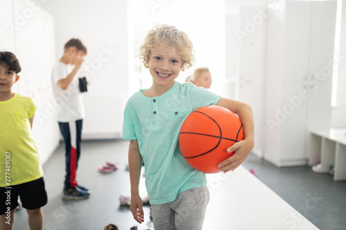 Smiling pupil holding basketball in changing room.