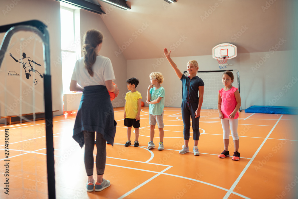 School girl raising her hand at sports lesson.