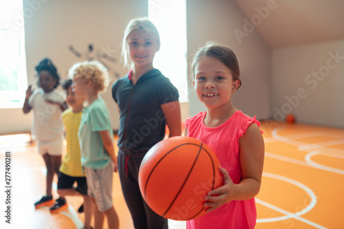 Little schoolgirl with a basketball standing near her classmates. © Viacheslav Yakobchuk