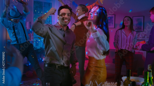 Photography At the College House Costume Party: Beautiful Girl and Boy Dance Together, in the Background Diverse Crowd of Young People Have Fun, Dancing, Jumping, Socializing and Drinking