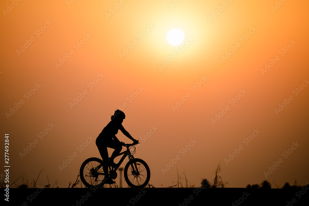 Silhouette woman cycling on sunset background