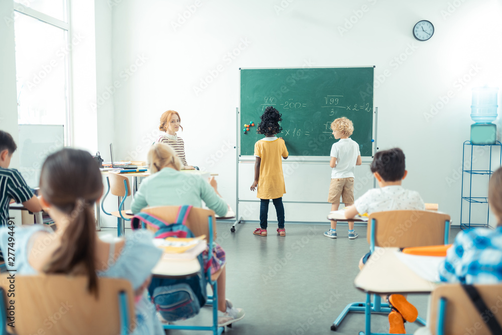 Teacher watching her class while two kids writing.