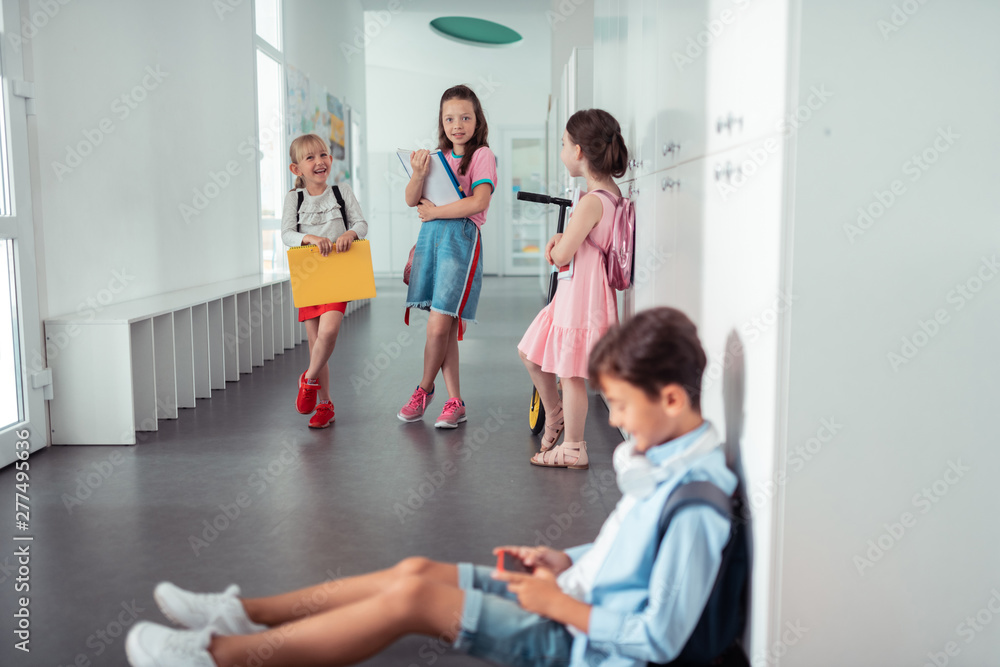 Girls standing and looking at boy sitting on the floor at school Girls standing and looking at boy sitting on the floor at school