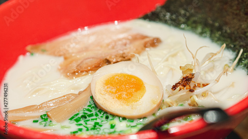 Closeup Shio or Salt-Flavored white soup ramen with boiled egg, braised pork, Negi, Menma, sprouting and dried seaweed in a red bowl.