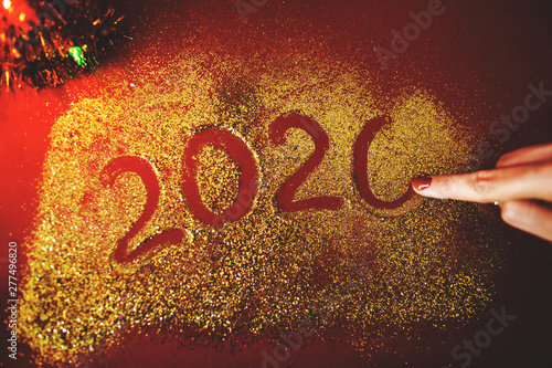 The woman's hand paint the figure of 2020 in the claret background with sparkles. New Year's concept