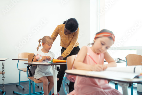 Helpful teacher wearing yellow blouse speaking with blonde girl