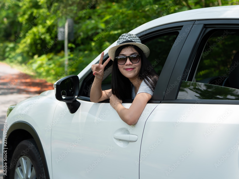 Happy asian women raising hands to summer holiday travel trip in the car on the road with sunlight, daylight and tree natural background. tourist vacation concept