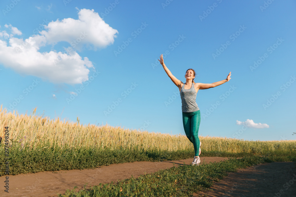 Happy woman on sunset or sunrise. Female runner raising arms expressing positivity and success.