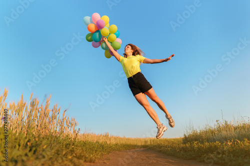 follow your dream  inspiration concept  young woman with colorful balloons jumping in summer field. fun  vacation  bright life