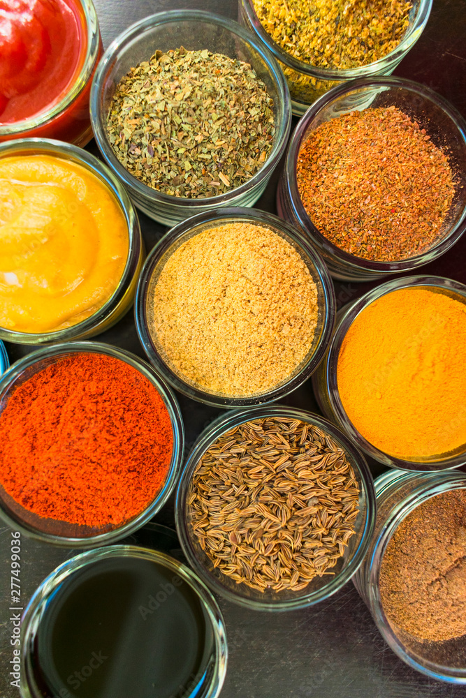 Set of spices and herbs. Indian cuisine Pepper, salt, paprika, curry, basil, mustard, nutmeg, turmeric. On a black wooden board. View from above. Close-up. Set of spices and herbs. Indian cuisine Pepper, salt, paprika, curry, basil, mustard, nutmeg, turmeric. On a black wooden board. View from above. Close-up.