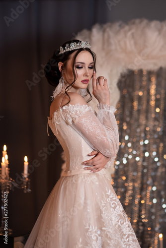 Portrait of the bride in the crown. With candles and a mirror. Lace dress. Large feather earrings. Hand on face.
