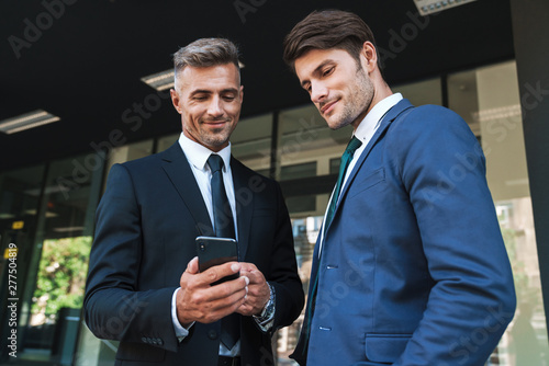 Portrait of professional businessmen partners standing outside job center and using cellphone together during working meeting photo